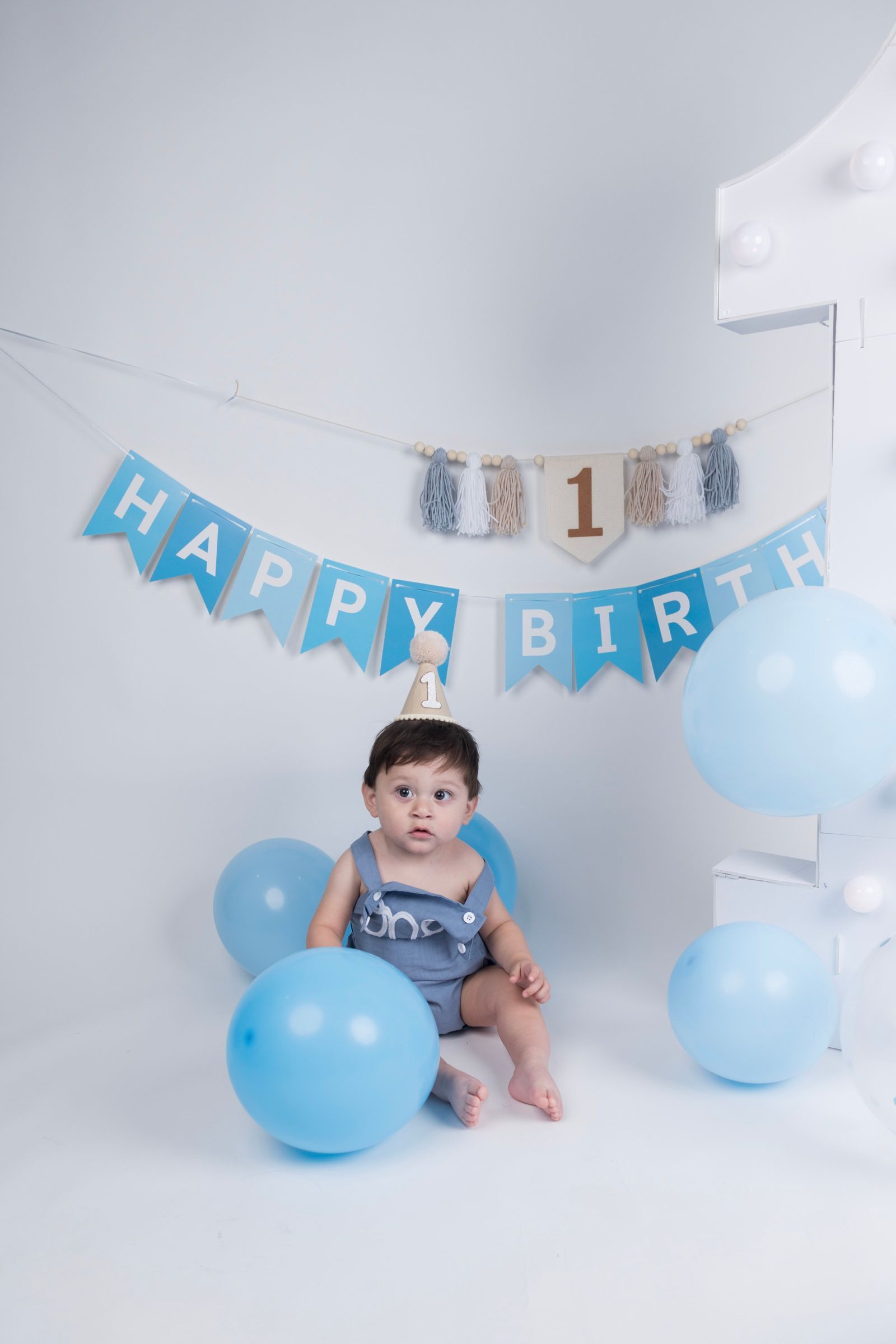 Baby celebrating a first birthday in a blue balloon studio set.