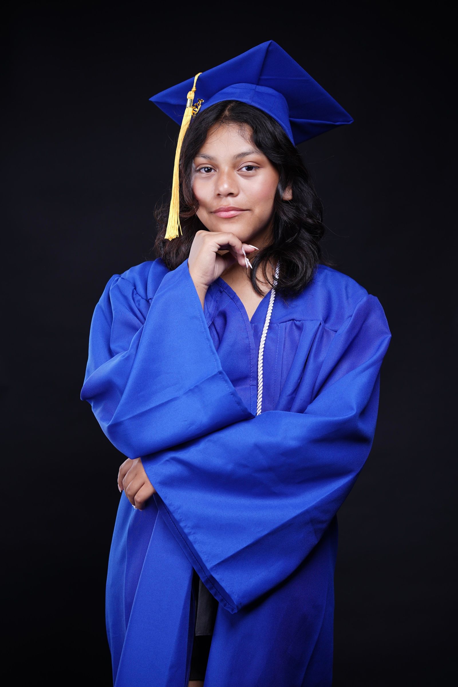 Graduate in a royal-blue cap and gown posing against a dark studio backdrop.