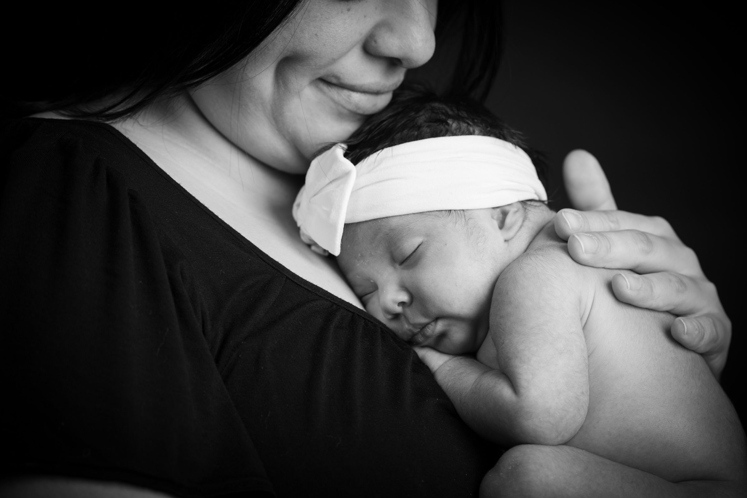 Mother holding her newborn in an intimate black-and-white portrait.